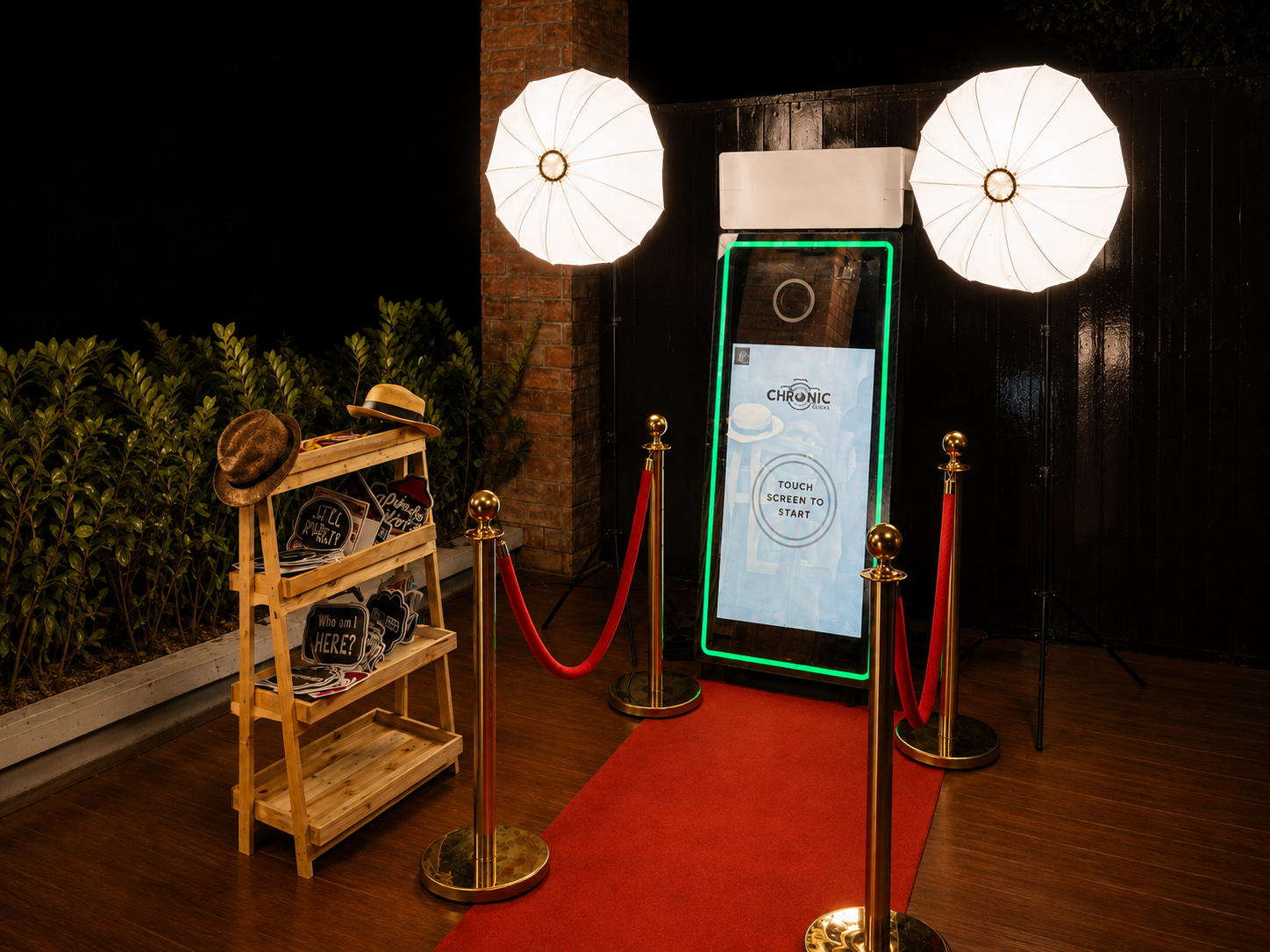 Chronic Clicks Interactive Mirror Photo Booth set up on a red carpet with ring light umbrellas and a props table